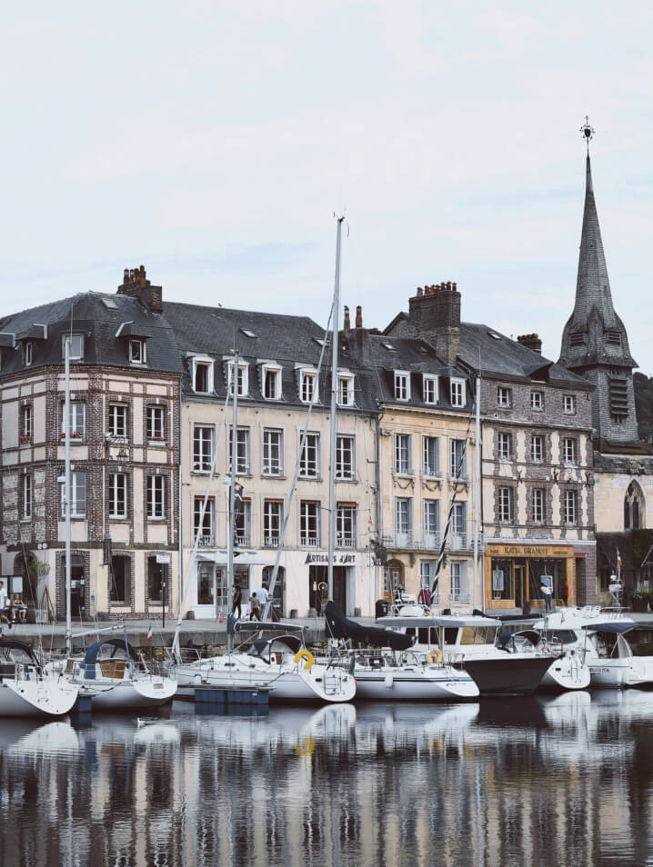 Port in Honfleur, France, with sailboats docked beside historic French apartments and a church in autumn.