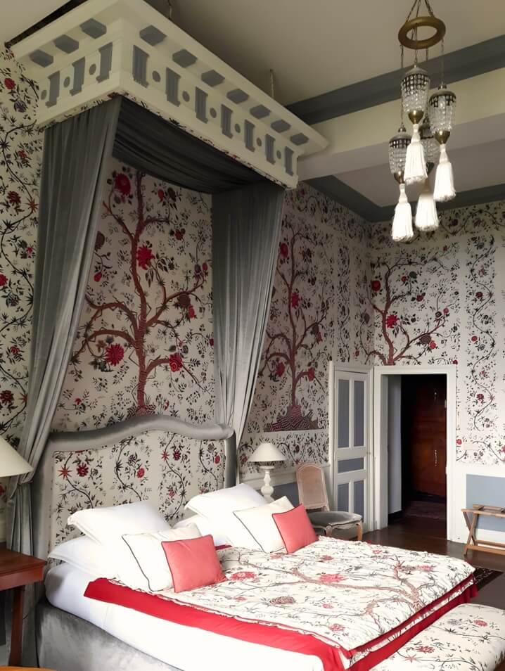 Elegant Brittany Ballue boutique hotel room with ornate wallpaper, matching bedding, and a bohemian chandelier.
