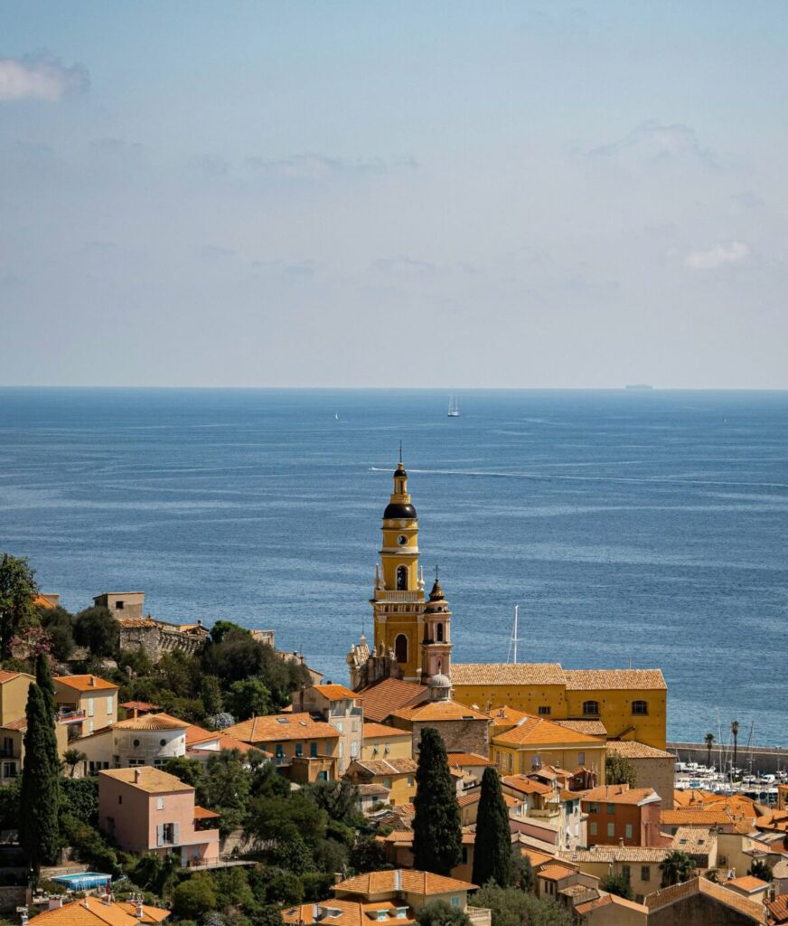 The French village of Menton on the French Riviera, overlooking the blue Mediterranean Sea with clear skies and boats in the distance.