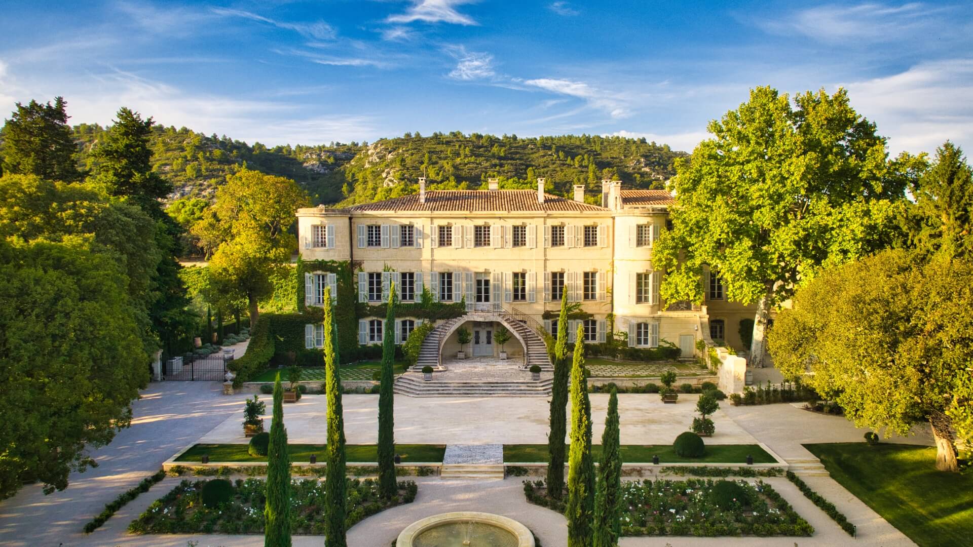 Estoublon vineyard in Provence, France, with lush, manicured grass, cypress trees, and green rocky hills in the background.