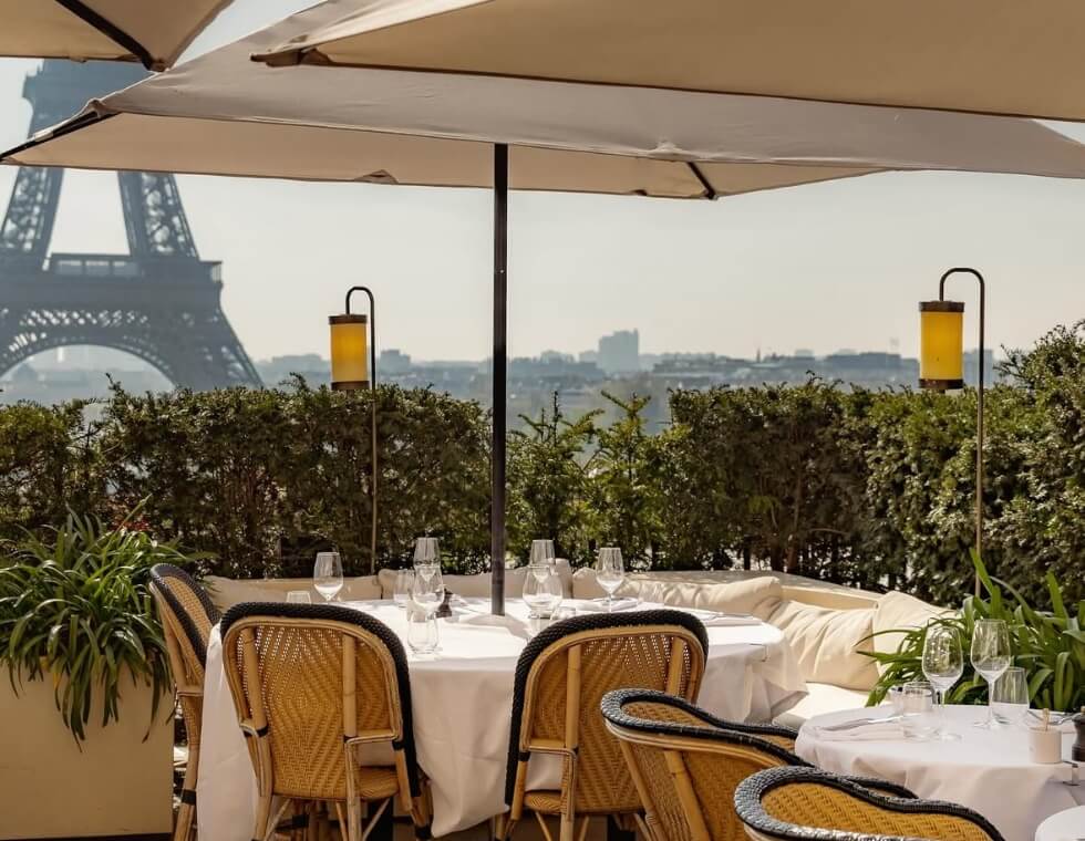 White dinner tables shaded by umbrellas on Girafe's rooftop, facing the Eiffel Tower.