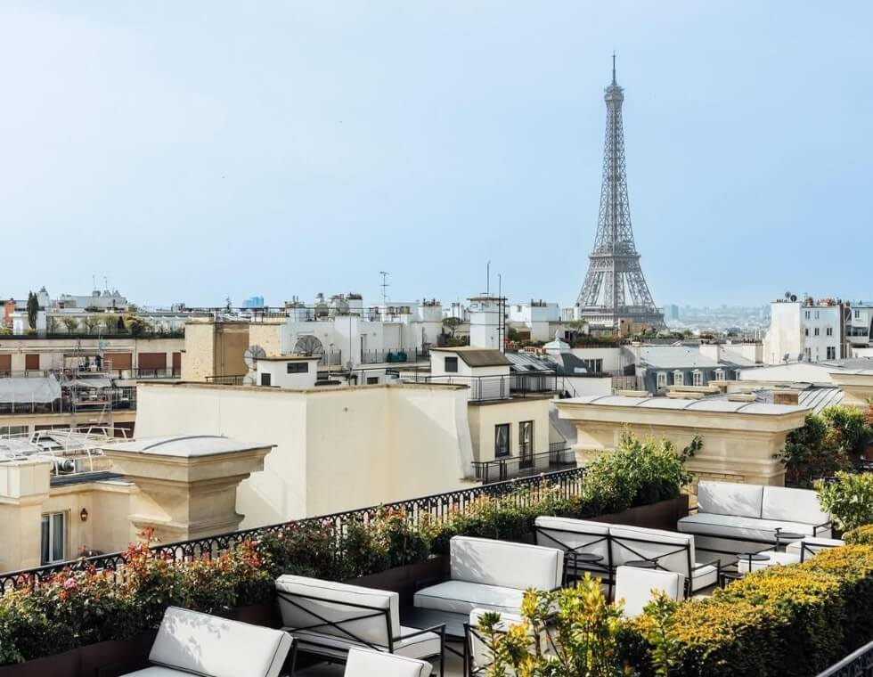 Rooftop view of Paris, with ample white benches and greenery, overlooking the Eiffel Tower.