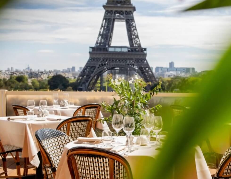 A rooftop lined with dinner tables, set for service, with the Eiffel Tower in the background.