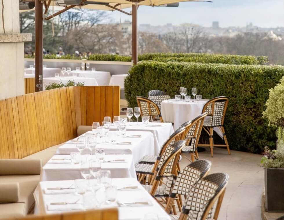 French bistro chairs and benches surround lunch tables on an outdoor rooftop terrace.