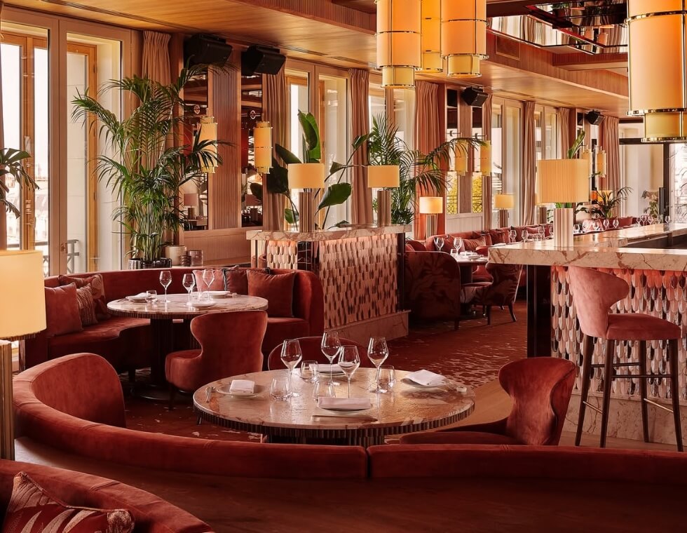Kinugawa restaurant interior decorated with velvet round-back seating, warm orange lighting, and tropical palms.