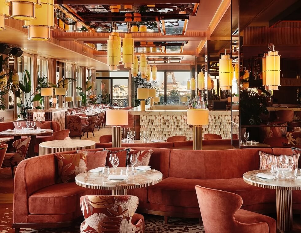 Warm lounge interior with orange velvet seating, lantern-style lighting, and palm leaves.