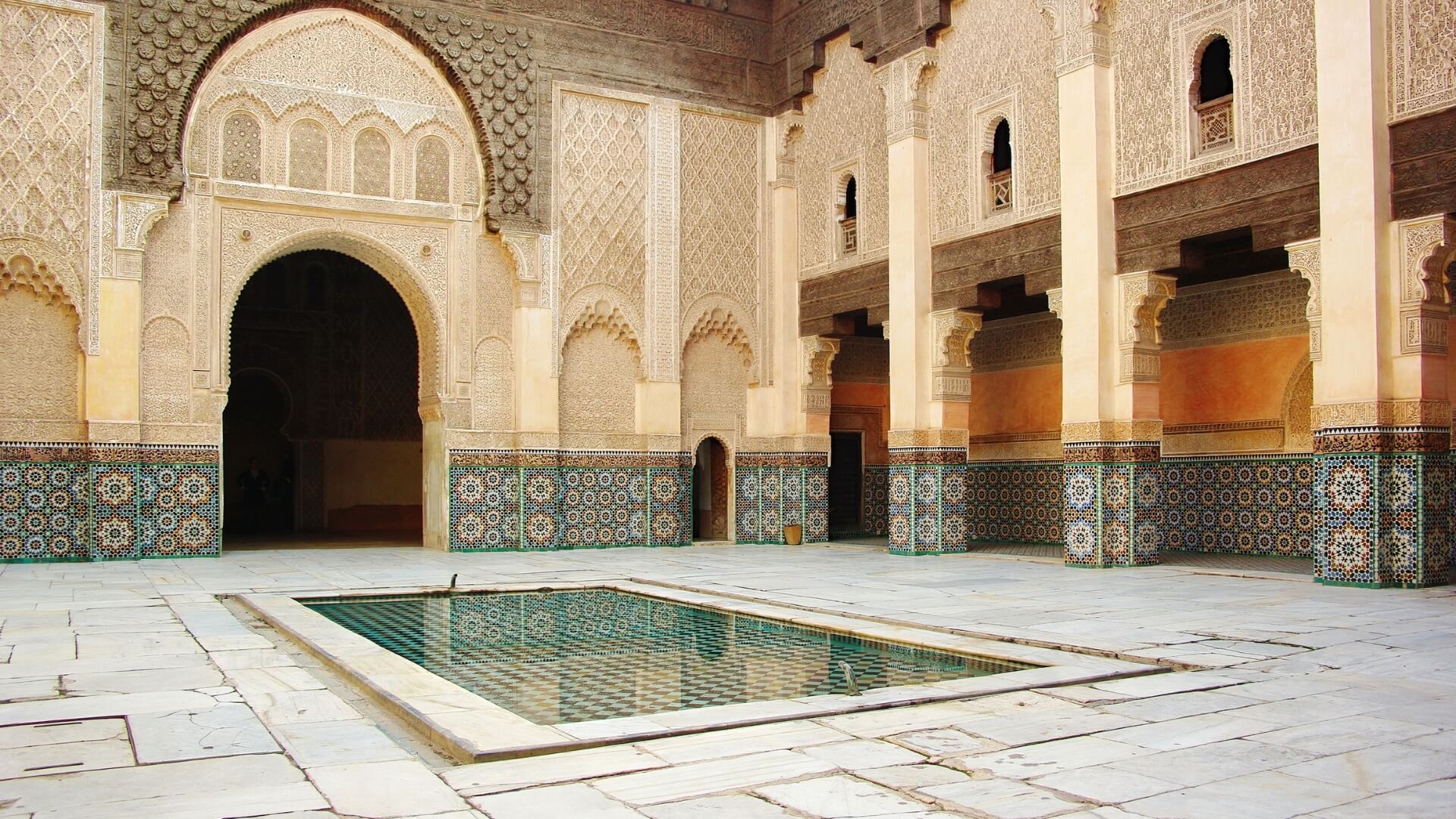 A tiled stone pool at the center of an ornate Moroccan courtyard.