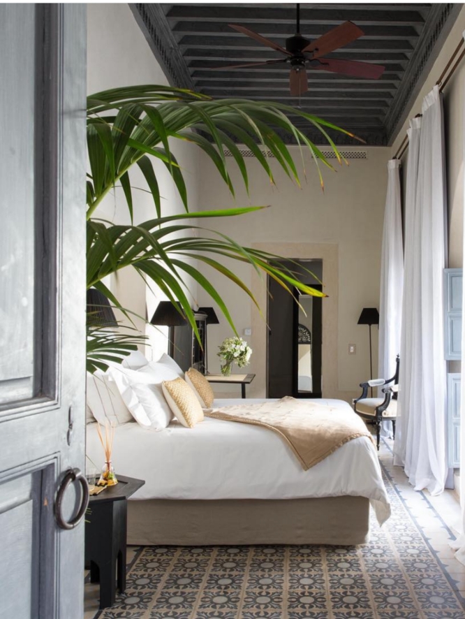 A lush, white bed, facing an open window, surrounded by minimal decorative accents.