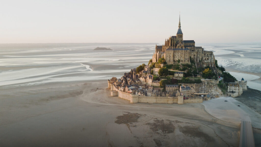 Mont Saint-Michel overlooking foggy coastal sands and tidal flats at low tide.