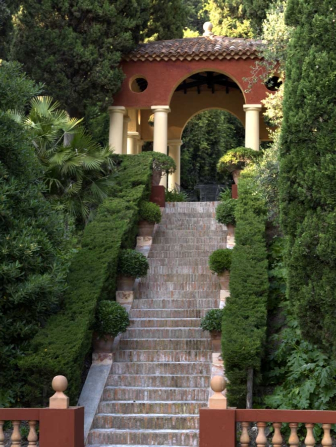 Garden steps at Colombières leading to a terra cotta column clad gazebo, covered in natural greenery.