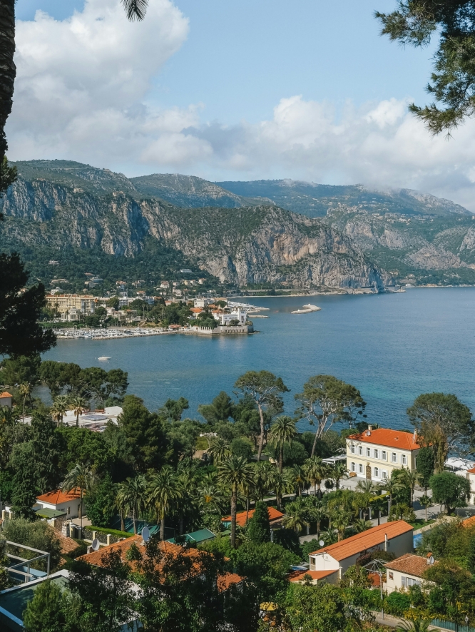 View from the Ephrussi estate in Saint-Jean-Cap-Ferrat overlooking topaz waters, sloping mountains, and blooming trees.