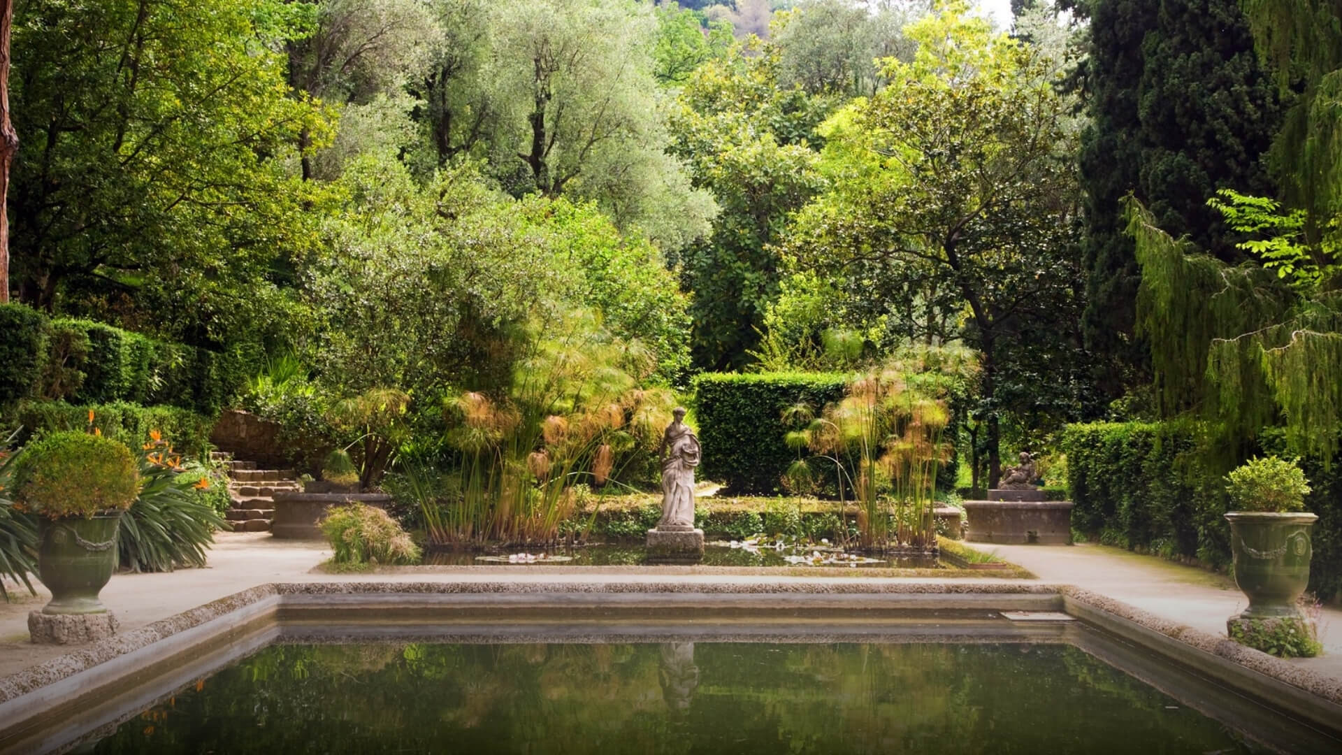 French Riviera garden with natural greenery, classical statues, and central stone ponds.