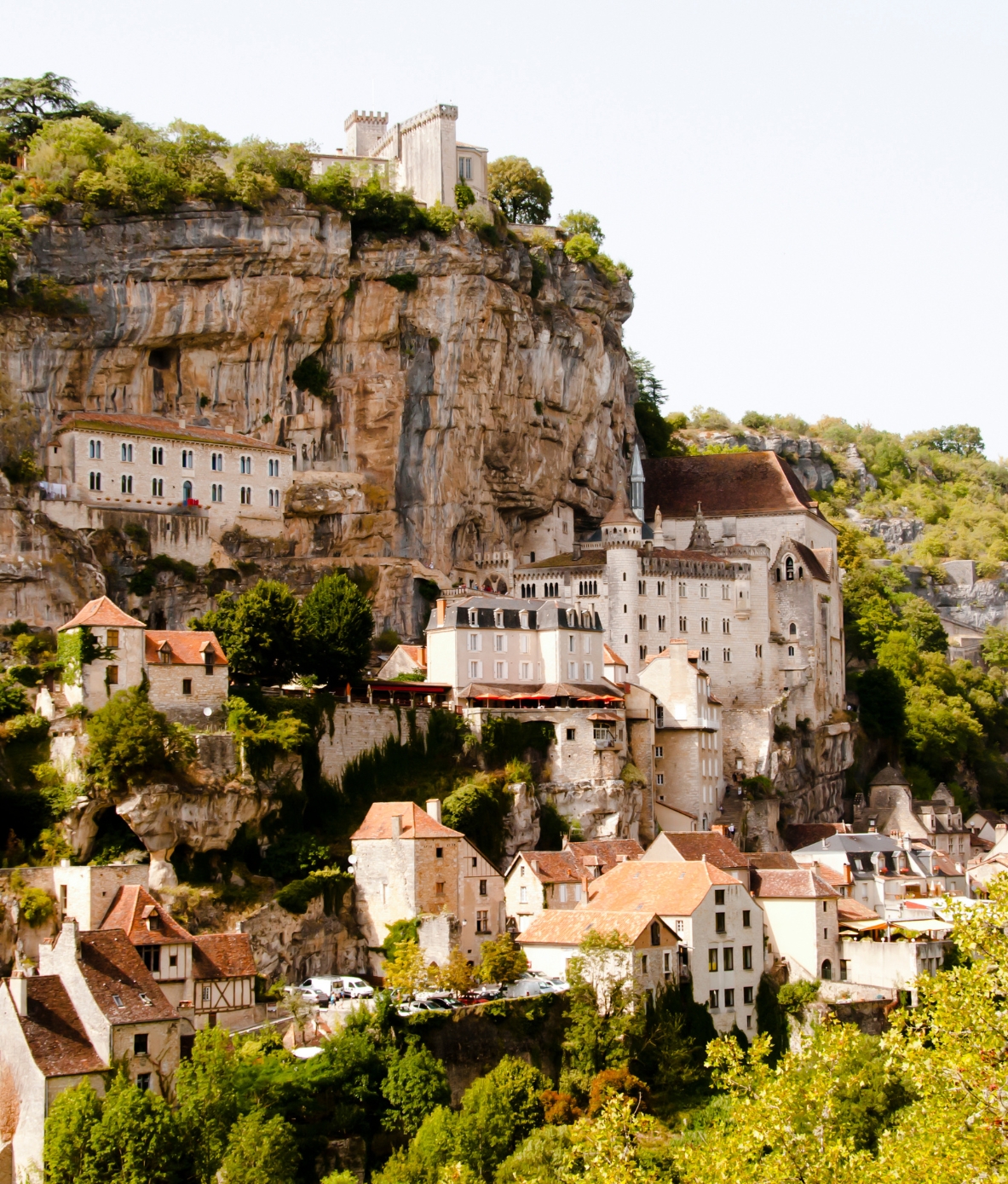 A mountainside village with homes clustered and stacked against a rugged cliff and surrounded by greenery.