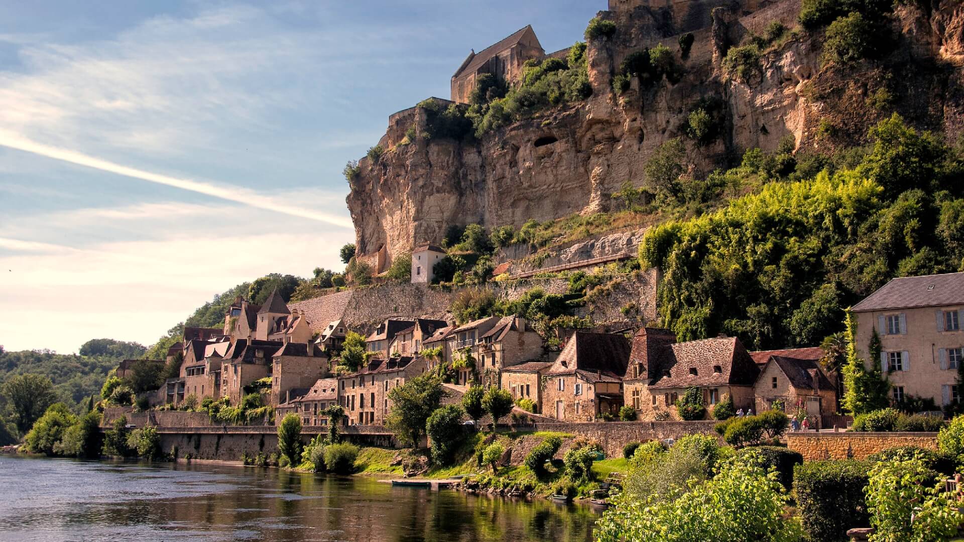 Cliffs of Beynac et Cazenac tower above a traditional stone village overlooking a flowing river.