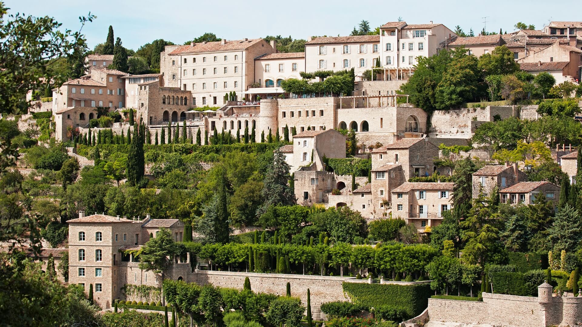 Mountainside village of Gordes in Provence, France, is covered in hilly walking paths bordered by cypress trees and lush green hedges.