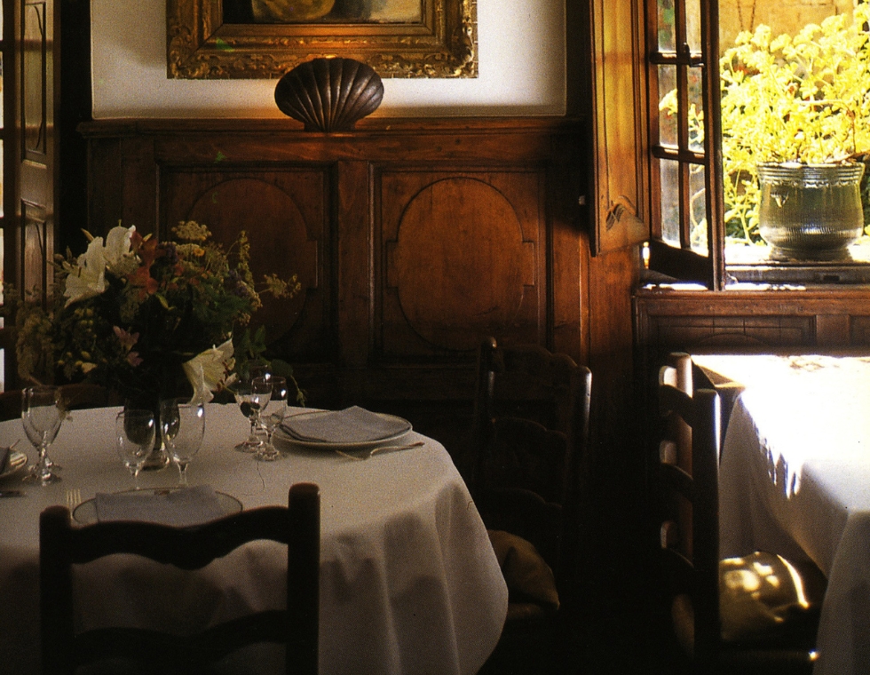 Simply set tables in La Colombe d’Or's dining room, featuring white linens and natural light, surrounded by elegant wood paneling.