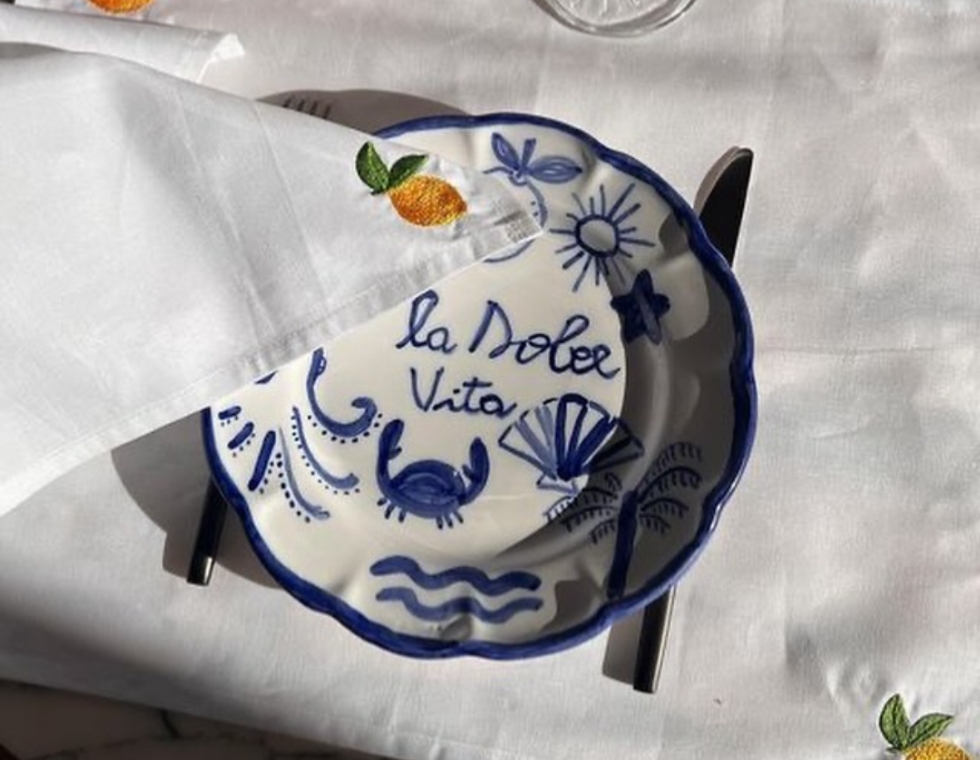 At La Pinede, a delicate hand-painted plate reading “La Dolce Vita” sits beside an embroidered napkin.