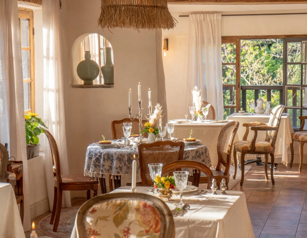 The interior of Le Chat Nobel restaurant on the Riviera offers small private tables set with crystal glasses, floral arrangements, and candlelight.