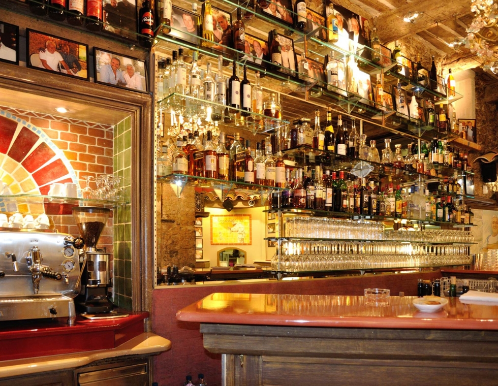 Warmly lit bar at Mamo Michelangelo in Antibes, stocked with a display of spirits and coffee, ready for service.