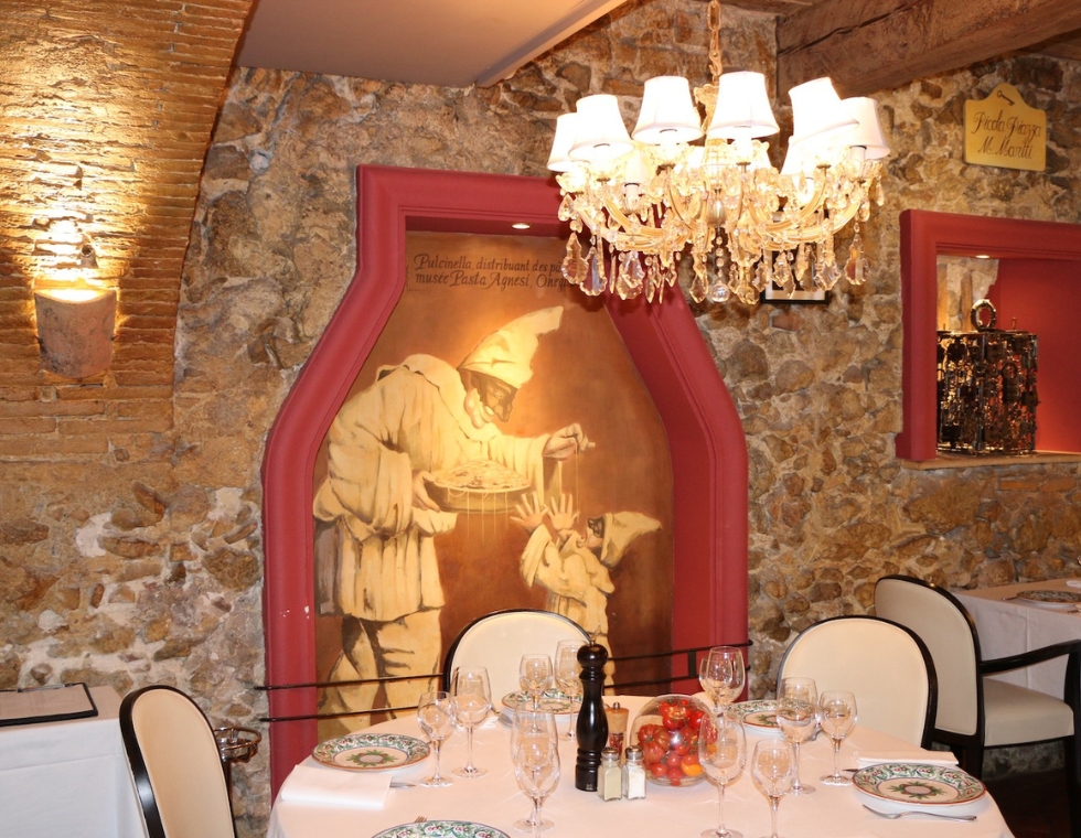 The warm dining room at Mamo in Antibes is lined with stone clad walls and framed frescoes.