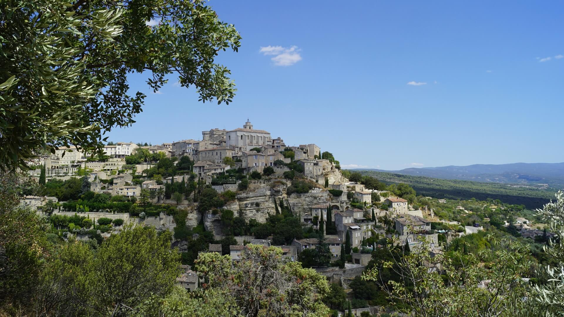 A clifftop town in the Alpilles region, framed by trees.
