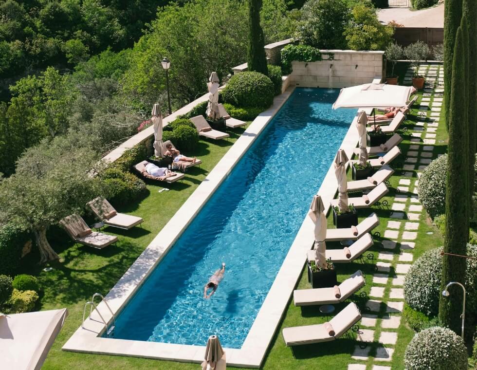 Turquoise swimming pool at Bastide de Gordes luxury hotel in Provence, set in a green courtyard with lounge chairs and trees.
