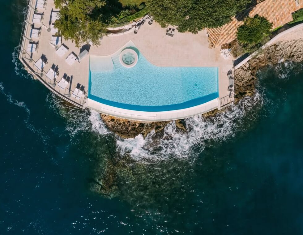 Cap Estel's luxury swimming pool on the rocky Provençal coastline, framed by lounge chairs with views of the Mediterranean Sea.