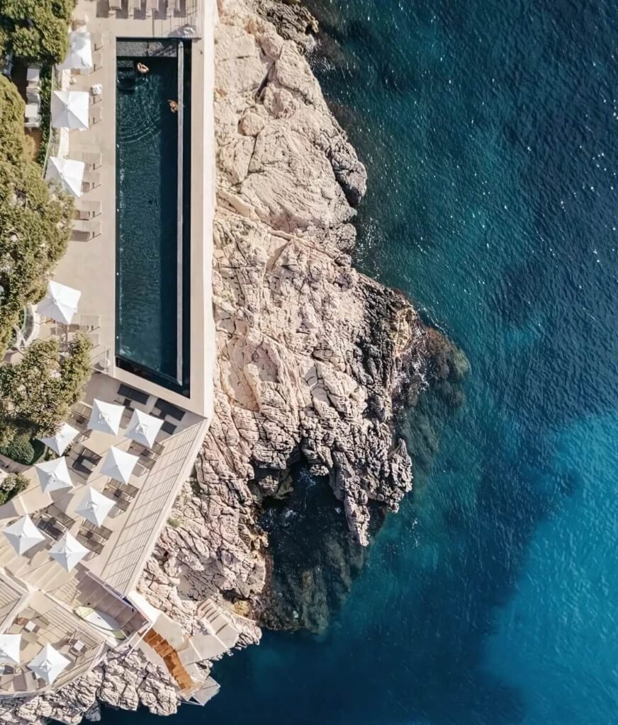 Aerial view of the Roches Blanches pool and the gem coloured Mediterranean Sea in Cassis, both glittering with vibrant blue hues.