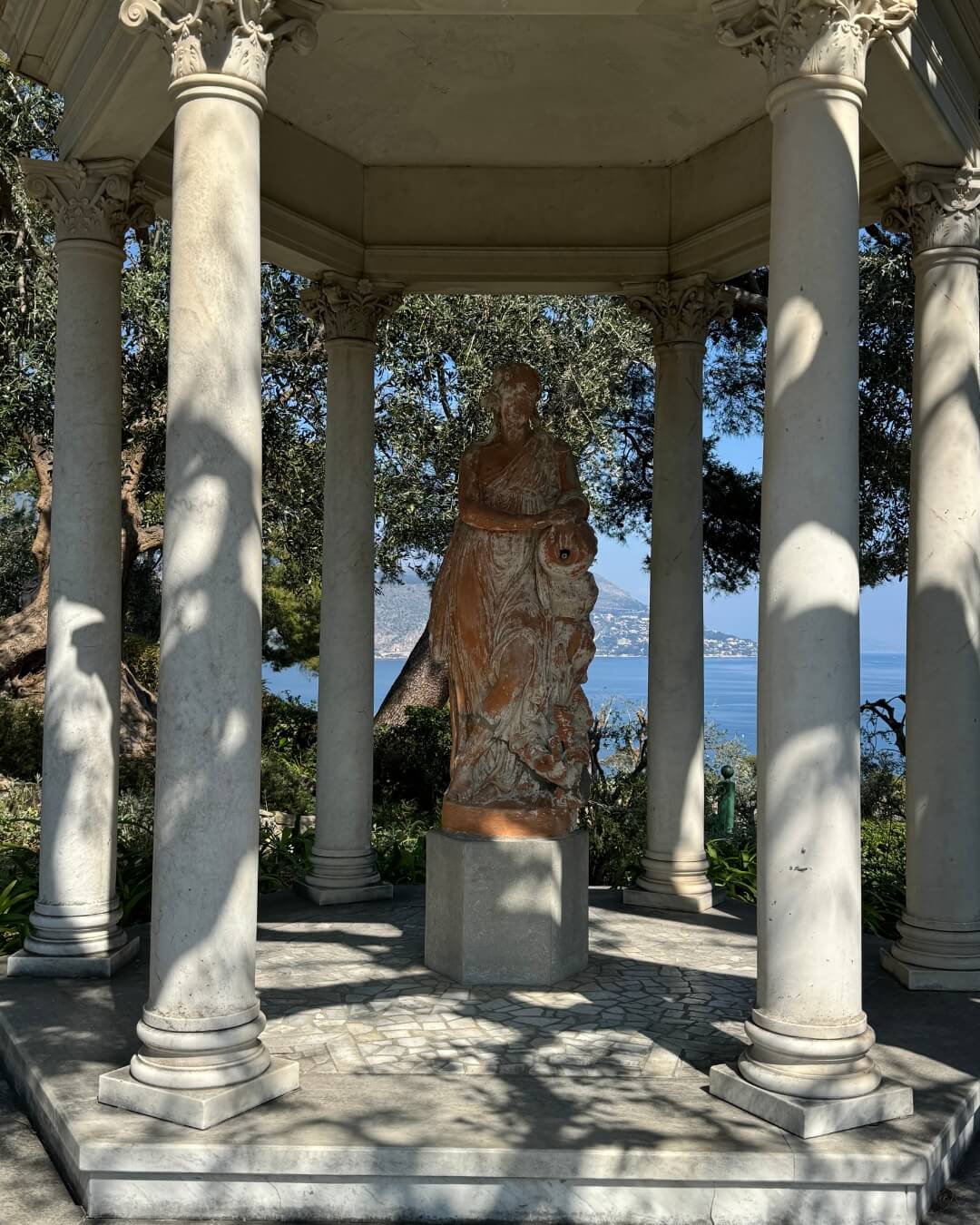 French Riviera garden gazebo featuring a mossy stone statue, overlooking the Mediterranean Sea.