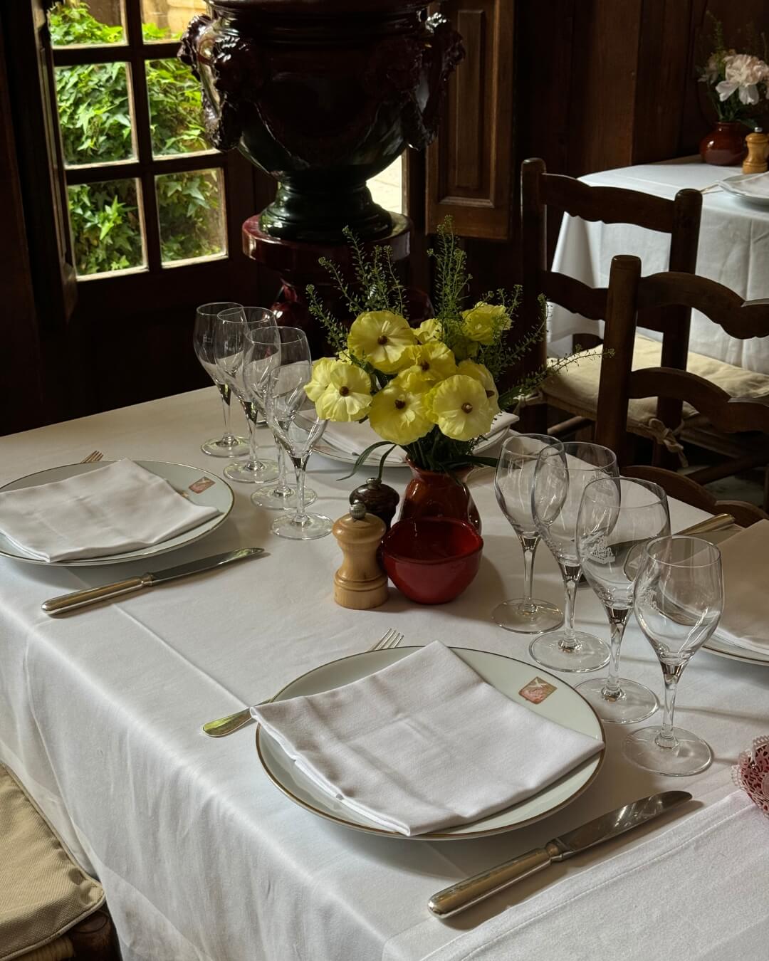 Simple French Riviera dining table set with linens and decorated with glasses, plates, and yellow flowers.