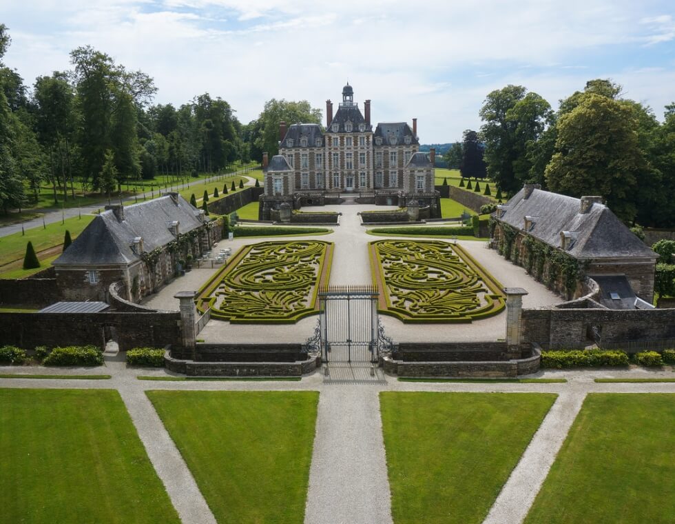 Château de Balleroy, set on rich green grounds, is enclosed by garden cottages, iron gates, and adorned with delicate labyrinth-style hedges.