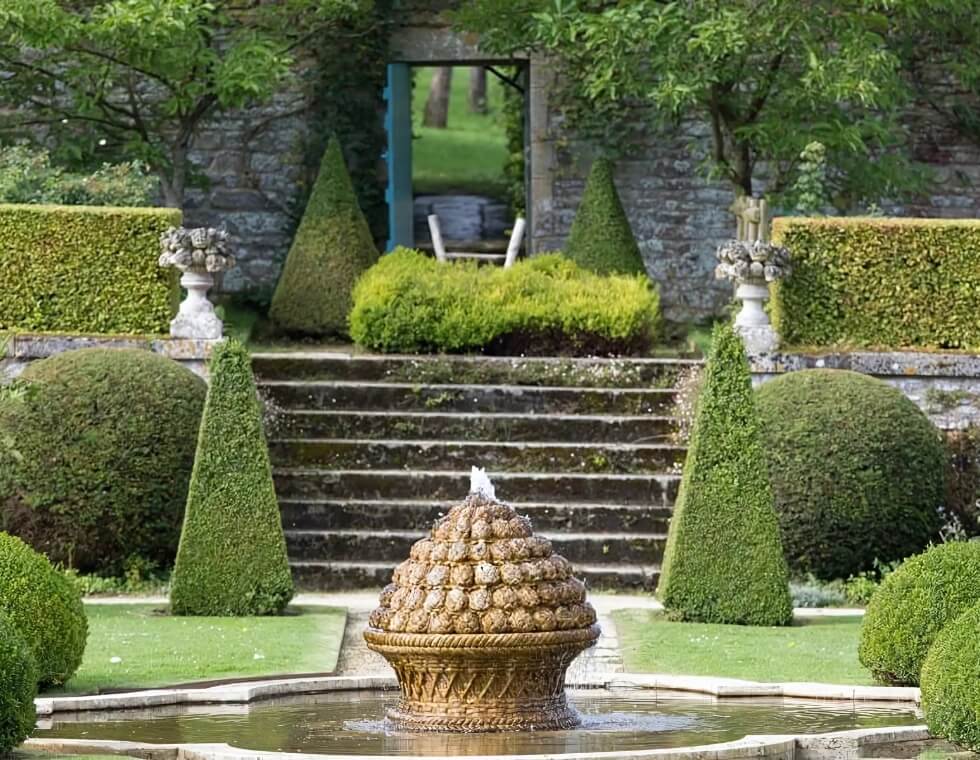 Bercy Castle’s courtyard features geometric hedges, ancient stone steps, and a diamond shaped pond.