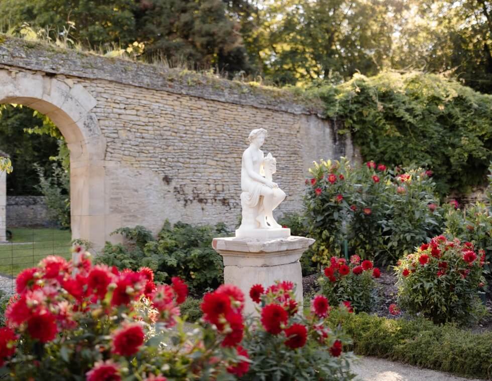 Canon Château’s gardens are lined with neatly placed blooming red flowers, bordering a marble statue and a stone wall.