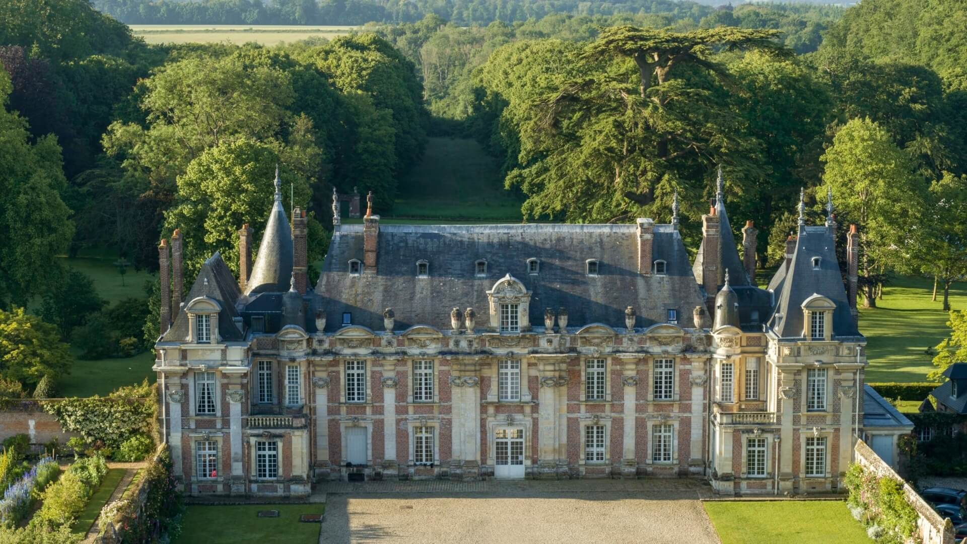 Château de Miromesnil, surrounded by sprawling green grounds, towering trees, and tended gardens.