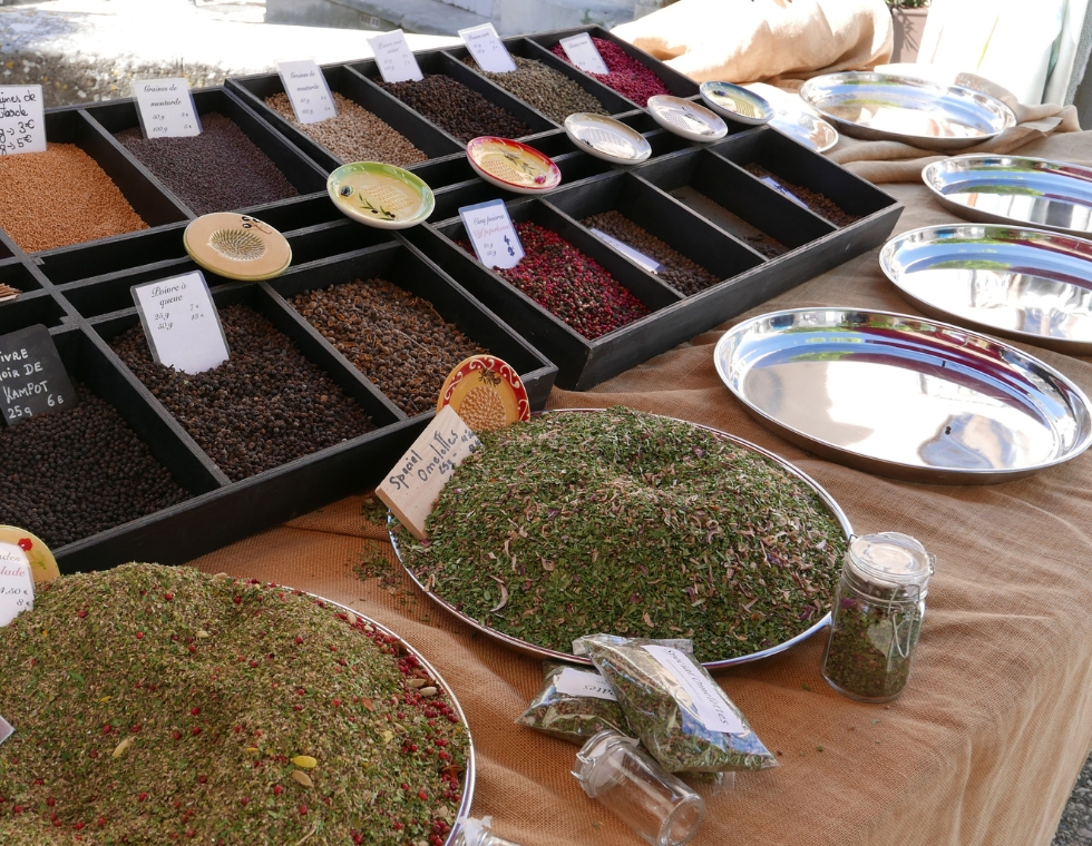 Silver trays of colorful Provençal spices and herbs packaged in glass jars at an outdoor French market.
