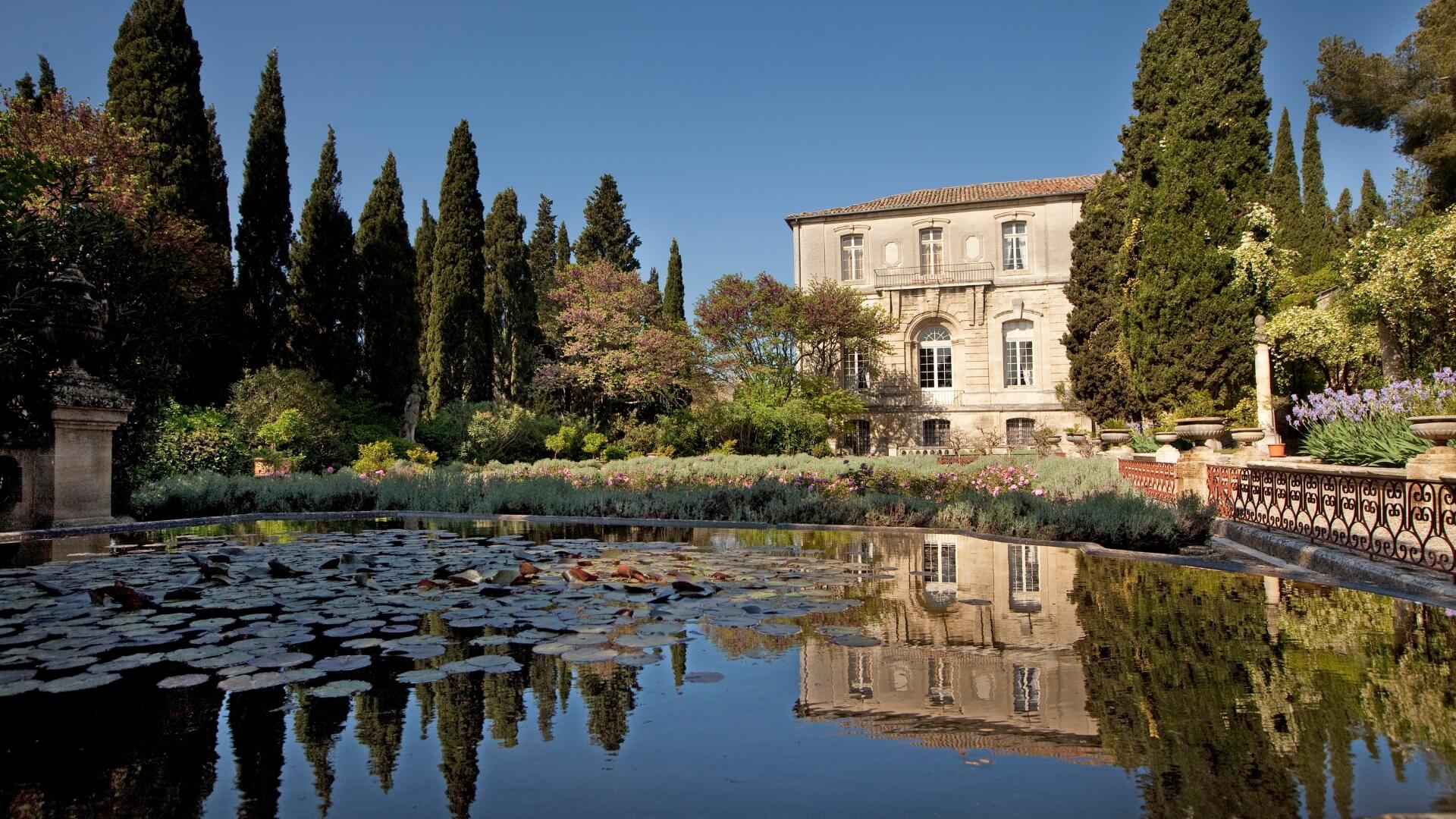 Abbaye Saint André garden lined with tall trees, lush greenery, and a lily pad covered pond.