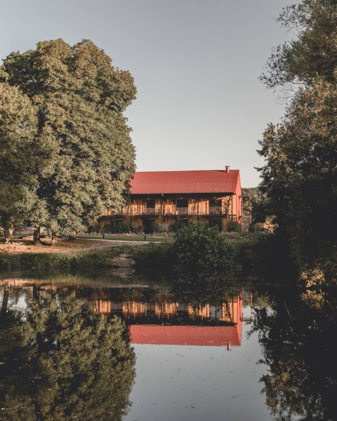Le Barn's countryside retreat features a pond framed by natural greenery and lush grass.