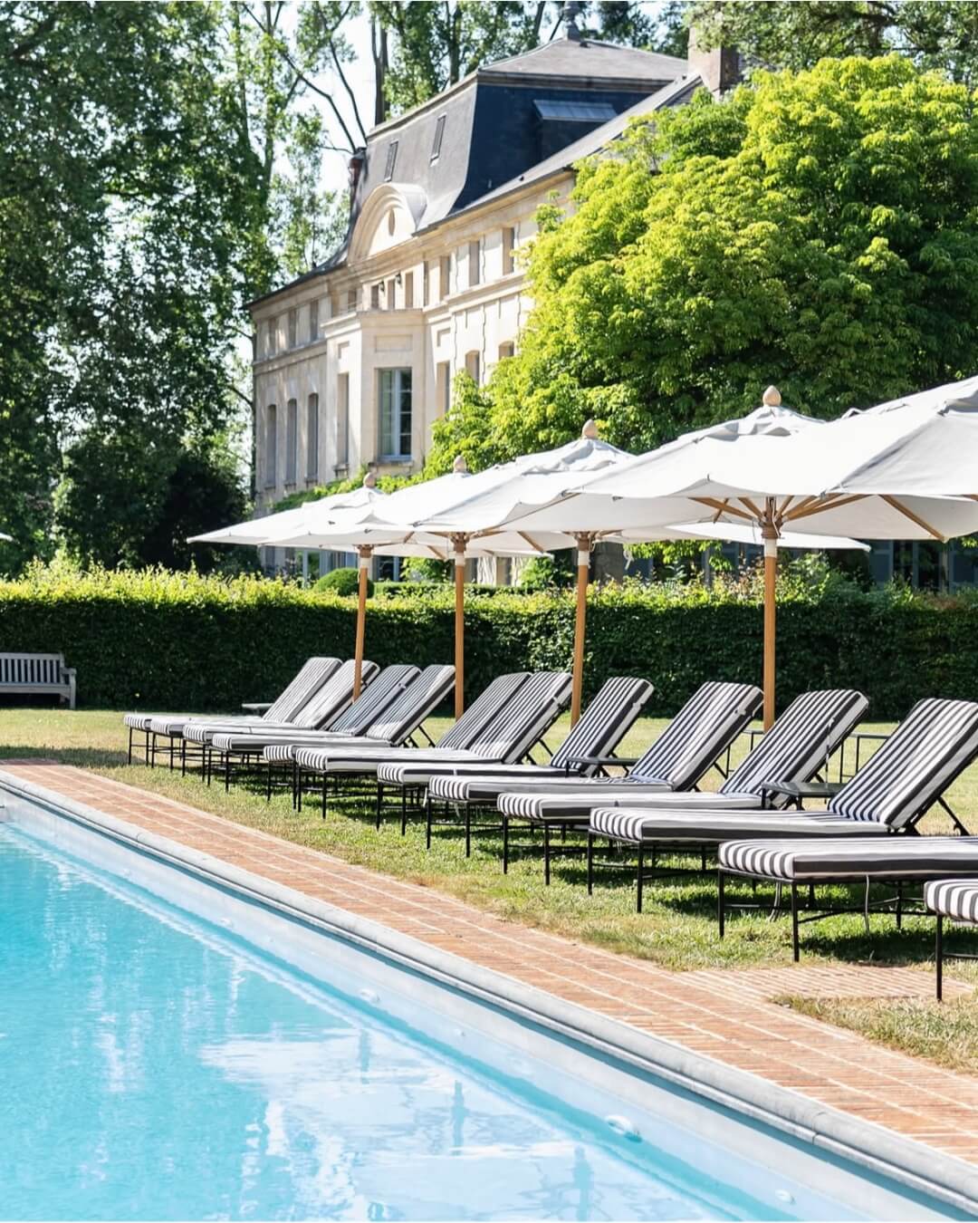 Domaine de Primard’s luxurious swimming pool is lined by hedges and black and white lounge chairs beneath white umbrellas.