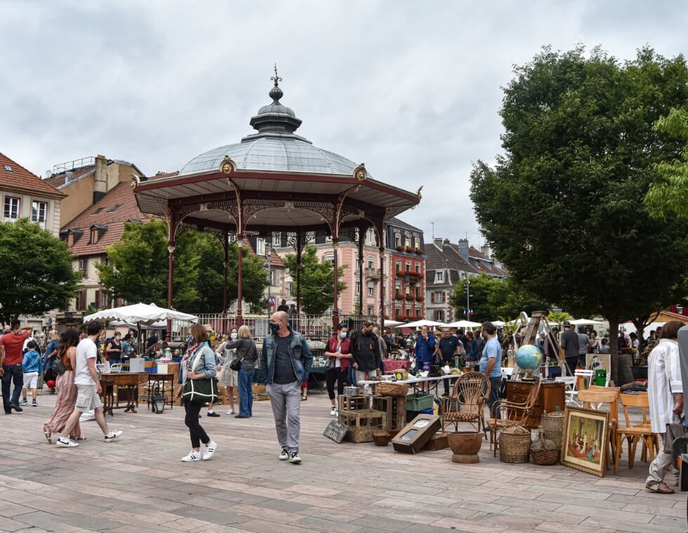 Lively French market in Annecy, featuring vendors, antiques, and a gazebo.