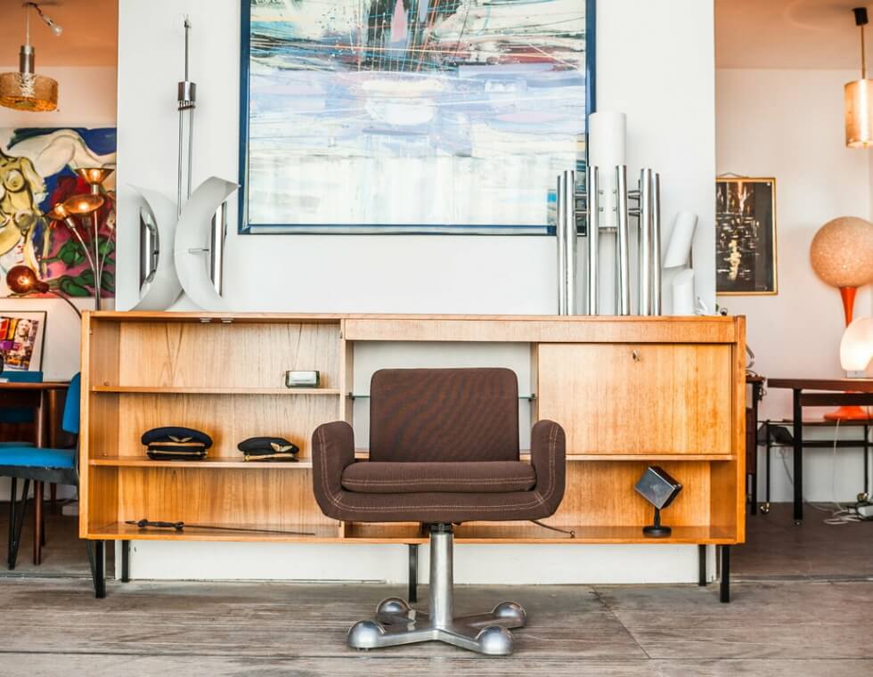 Mid century modern brown rolling chair, shelves, and home decor at Les Puces du Canal flea market in France.