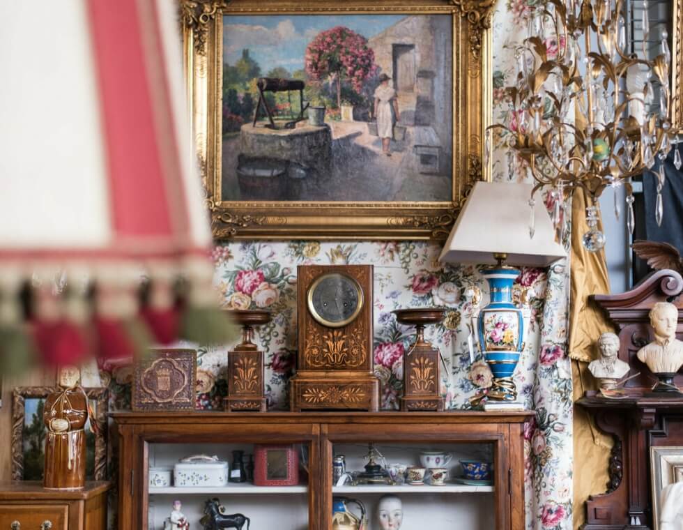 Antique painting, clock, and light fixtures against floral background in Les Puces du Canal market.