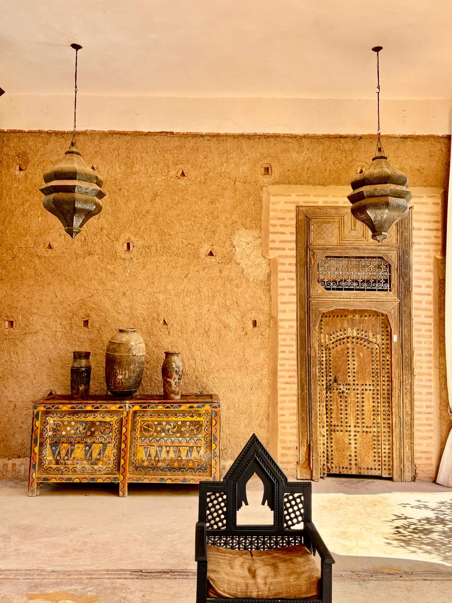 Rustic interior of a Moroccan style room, filled with natural light, hanging lanterns, and ornate furniture.