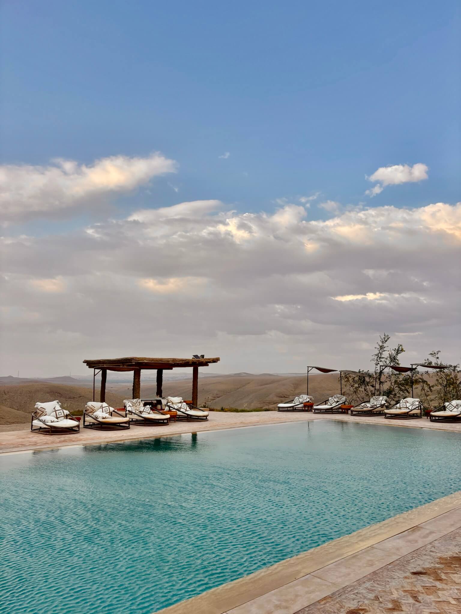 Luxury swimming pool in desert setting, surrounded by mountains and white lounge chairs.
