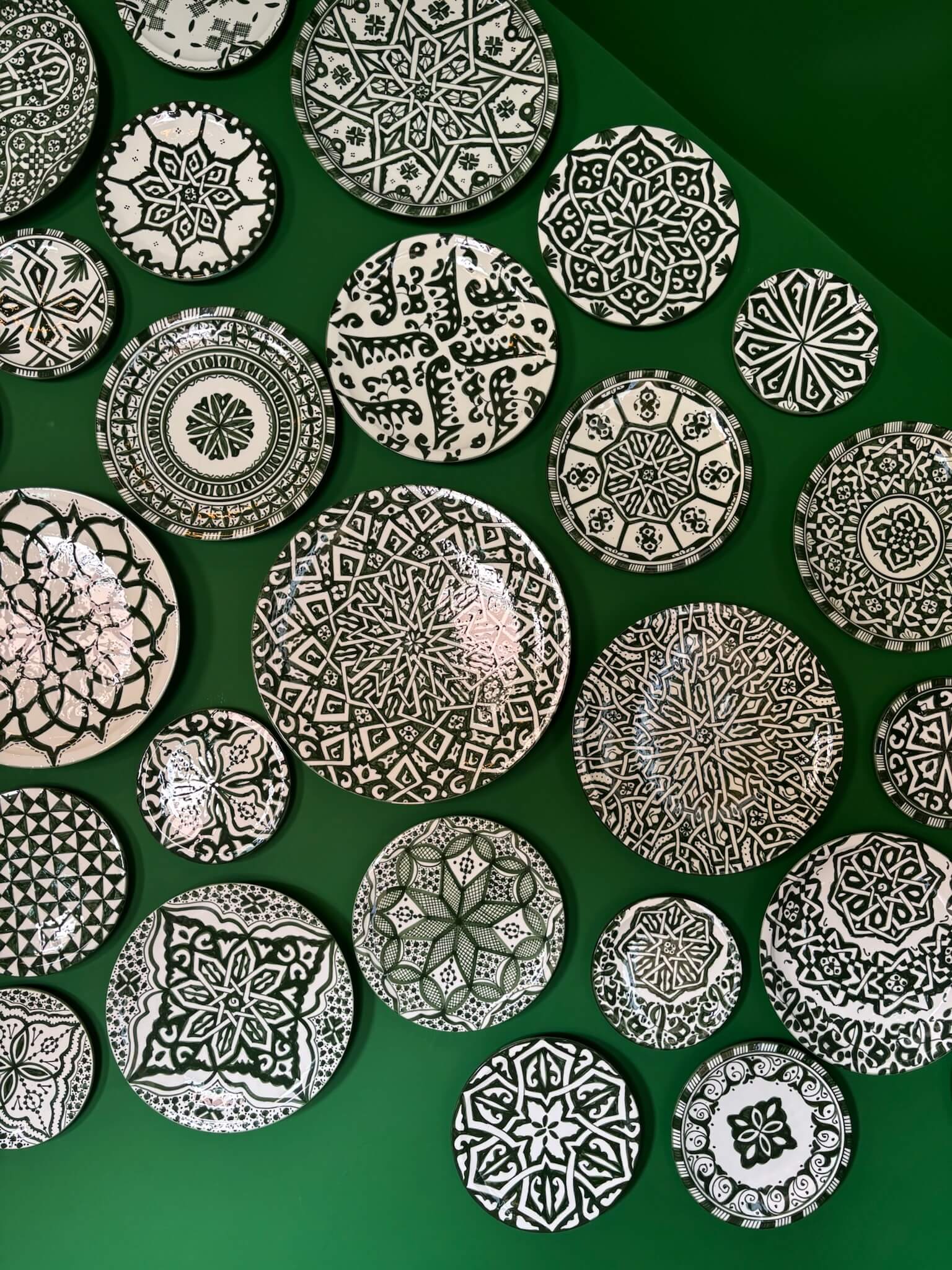 Ornate Moroccan green and white painted plates organised on a green table.