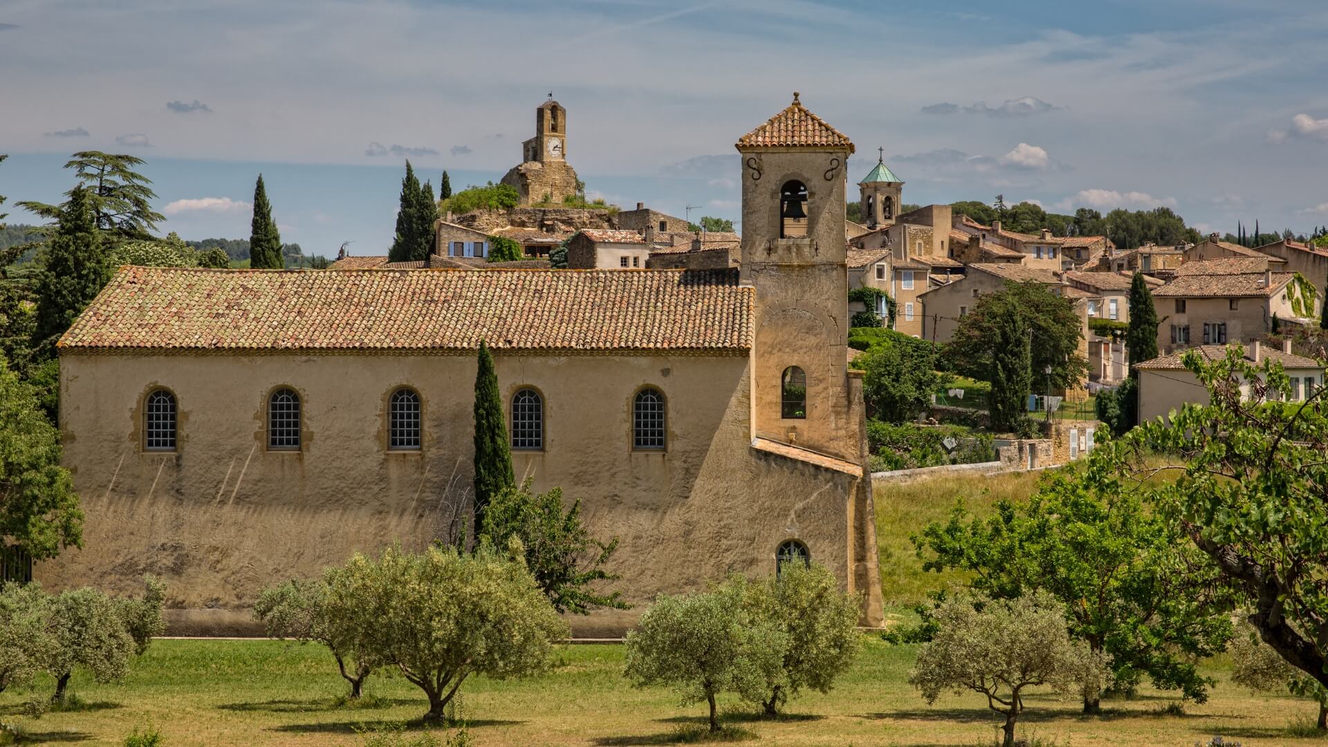 Lourmarin, a Provençal village in southern France, features a simple church surrounded by olive groves and lush Mediterranean greenery.