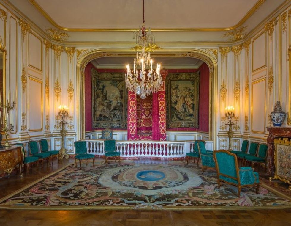 Historic interior of Chambord Castle, featuring Louis XVI decorative accents, gold moulding, antique furniture, and a crystal chandelier.