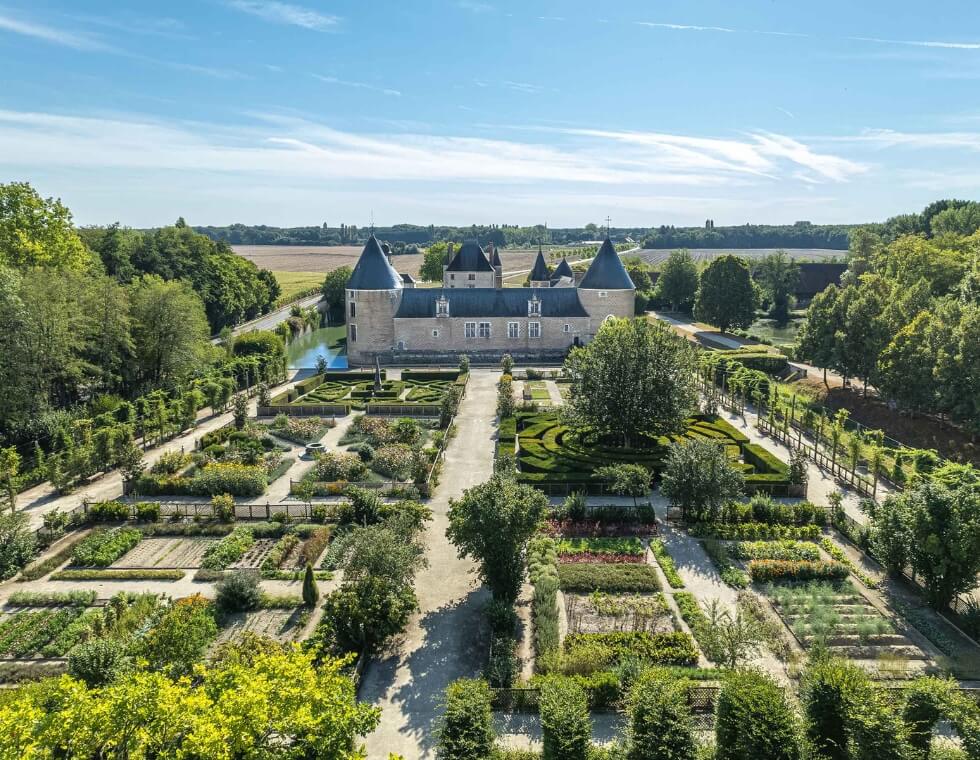 Medieval Chamerolles Castle in Chilleurs-aux-Bois, France, with lush green vegetable gardens.