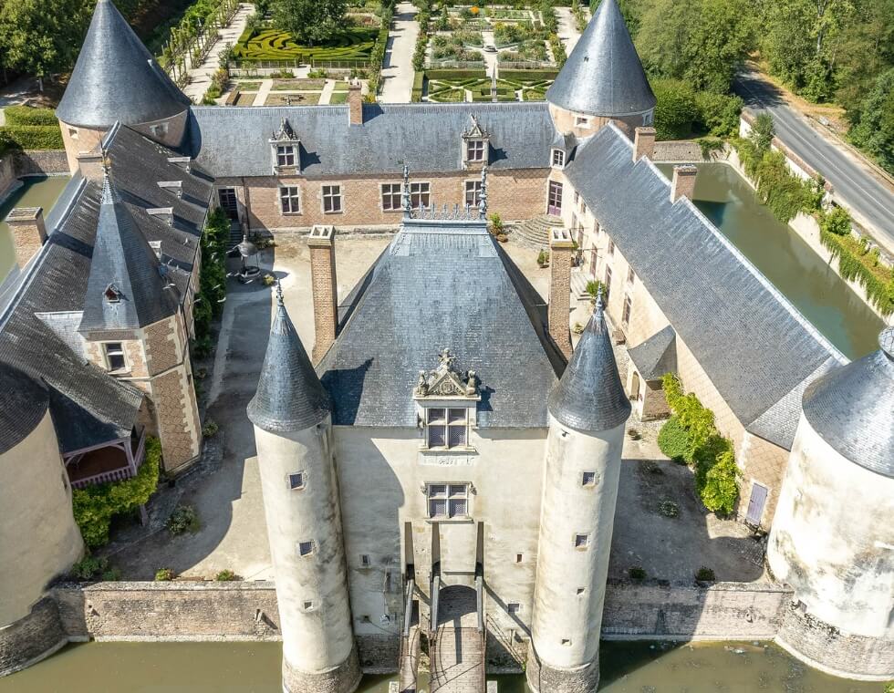 Aerial view of historic Chamerolles Castle in Chilleurs-aux-Bois, France, surrounded by a moat and lush traditional gardens.