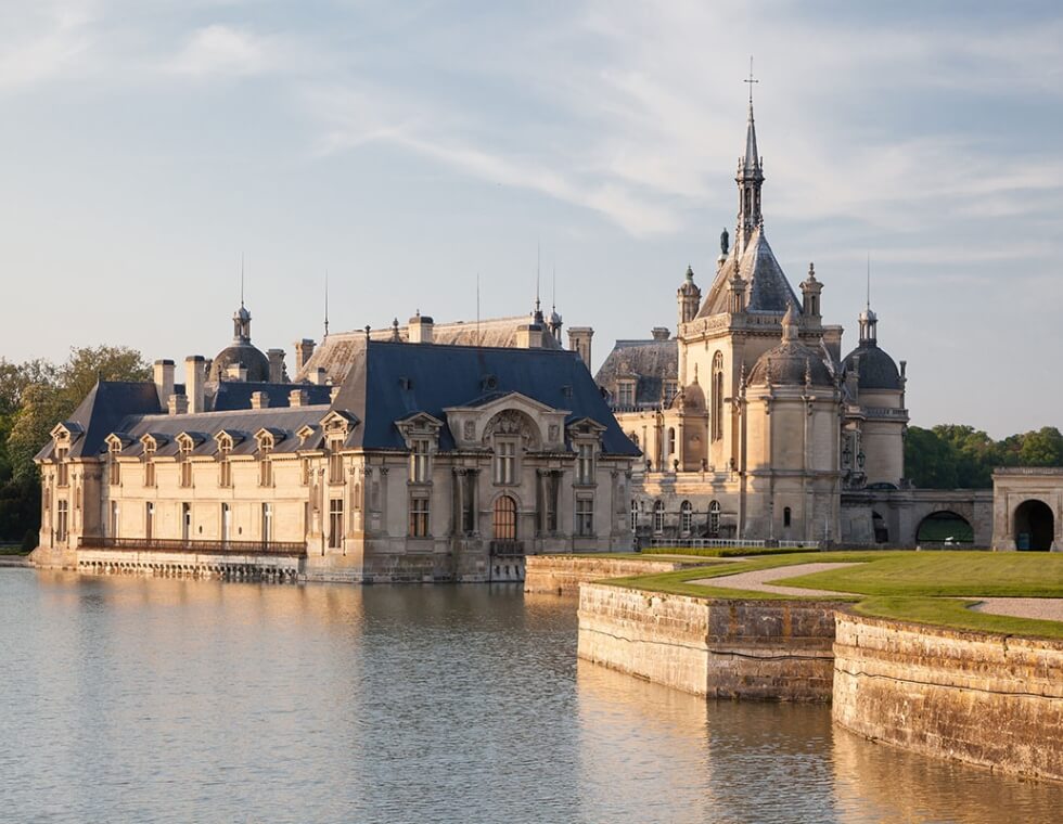 Chantilly Castle estate grounds in Chantilly, France, featuring a body of water beside a lush walking path.