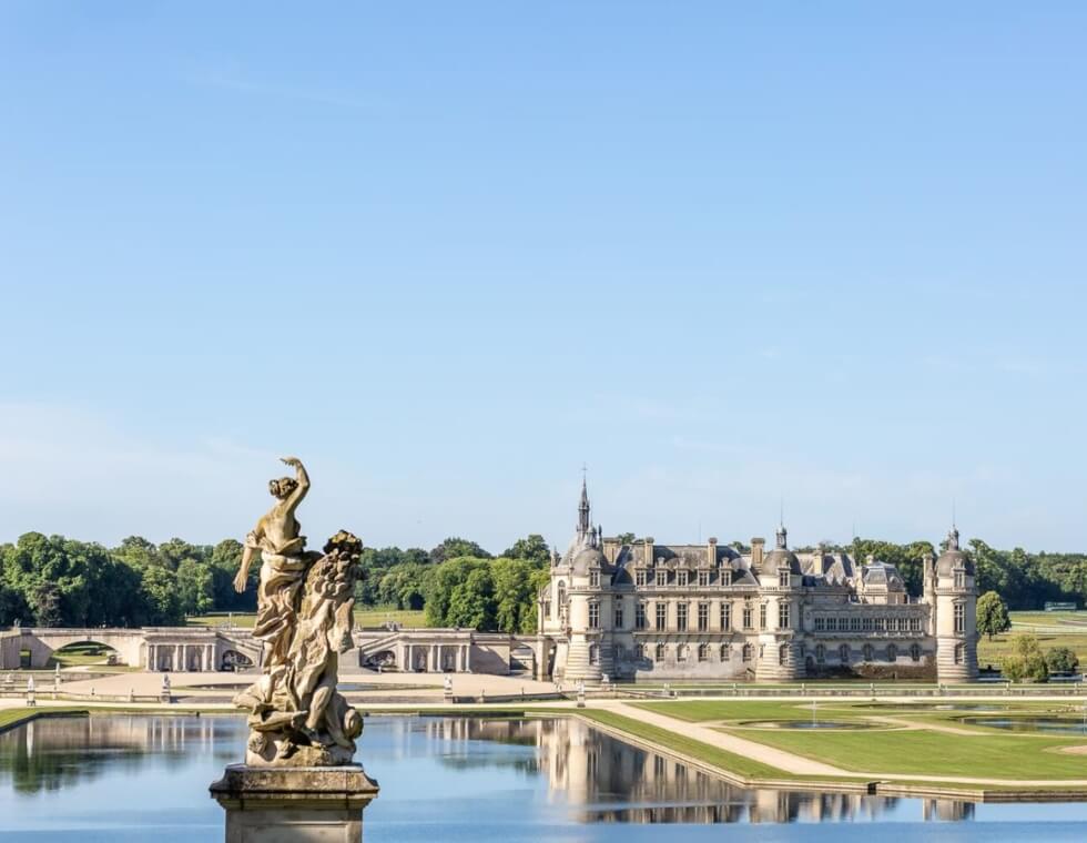 Chantilly Castle estate grounds with a pond featuring carved stone statues at the center.